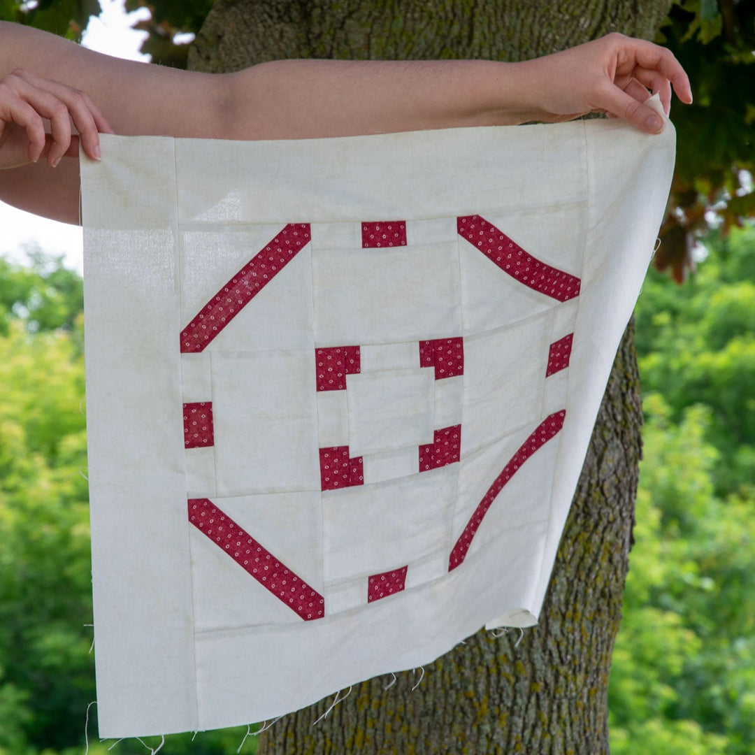 Person holding a quilt square with red geometric patterns against a tree