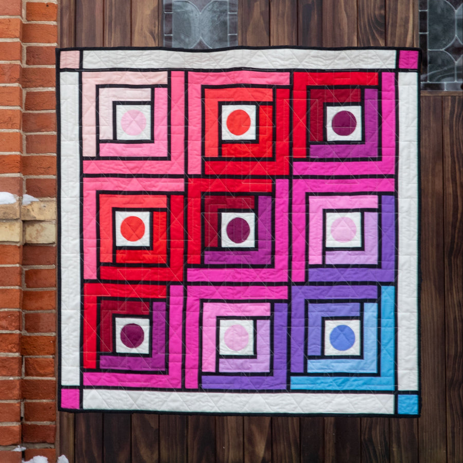 Colourful quilt displayed on a door of St. Mary's Catholic Church with brick wall and snow.